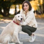 A young woman crouching beside her Golden Retriever on a park pathway in autumn, representing responsible female dog ownership and the importance of spaying and reproductive health care for dogs.